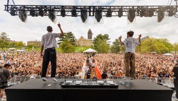 Two performers seen from backstage, facing the crowd on the Slope. 